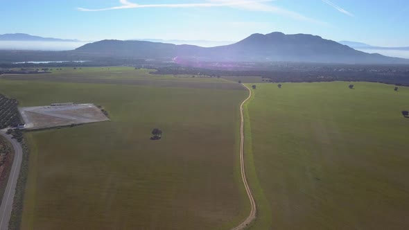 Aerial view of an extense meadow in a sunny hazy day with mountains in the background.