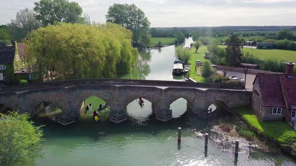 Group Of People Paddling Kayak And Passing Under The Stone Bridge In River Thames With Green Nature 