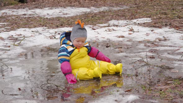 Cute Child in Yellow Waterproof Rain Pants Bibs for Kids and Rubber Boots on a Walk in Park in Early