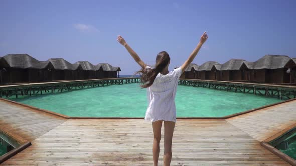 Beautiful sexy lady in white dress resting in Maldives. Walking on pier near water bungalows.