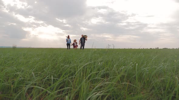 Family Farmers Are Walking Along the Field at Sunset, Carrying Box with Fresh Vegetables and Tools