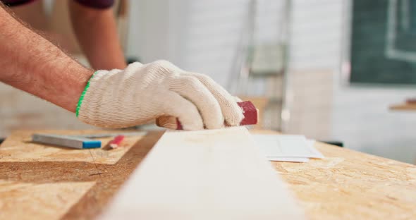 A Bearded Handyman is Sanding Wood for Furniture in a Carpentry Workshop The Carpenter Blows Off the