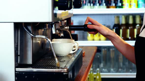 Waitress making cup of coffee at counter in kitchen