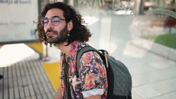 Pretty curly-haired bearded man in eyeglasses looking around and texting on phone