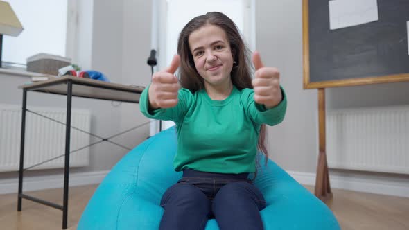 Front View Cheerful Little Person Gesturing Thumbs Up Looking at Camera Smiling Sitting on Bag Chair