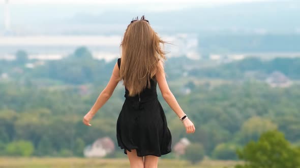 Young Happy Woman in Short Black Dress Standing on Hill Top Enjoying Warm Summer Day