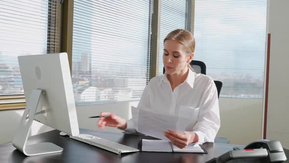 Female Manager Reads Documents and Financial Reports Sitting at the Workplace and Typing Text on the