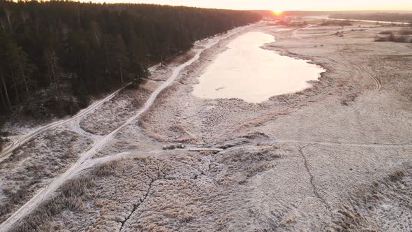 Field Forest and Lake Under the Snow in the Orange Light of the Sun