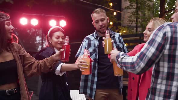 Group of Likable Slender Youth Having Fun Together and Clinking Bottles of Non-Alcoholic Drinks 