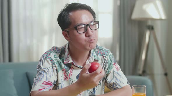 Close Up Of Happy Asian Man Biting An Apple While Having Healthy Food At Home