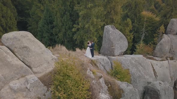 Newlyweds Stand on a High Slope of the Mountain. Groom and Bride. Aerial View