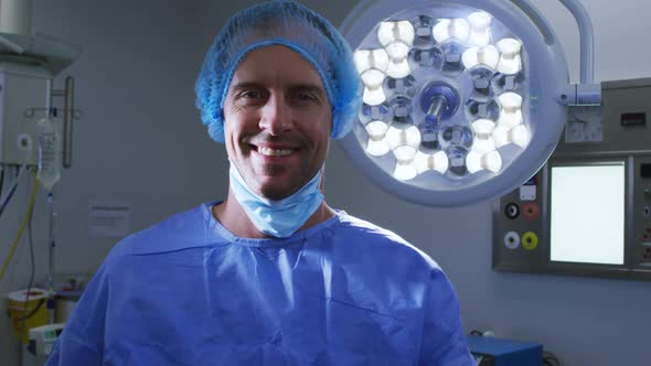 Portrait of smiling male caucasian surgeon with face mask and scrubs in hospital