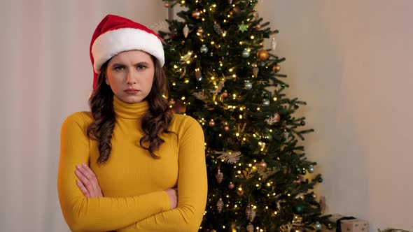 Portrait Upset Young Woman in Santa Claus Hat Crosses Hands Looks Camera at Home