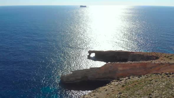 Drone shot over rocks in nature and towards a natural stone window on the Mediterranean sea of Malta