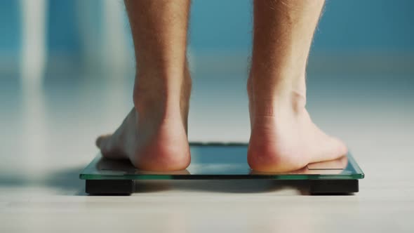 Bare male legs, steps on the scales, is weighed and walks away, healthy eating, weight loss