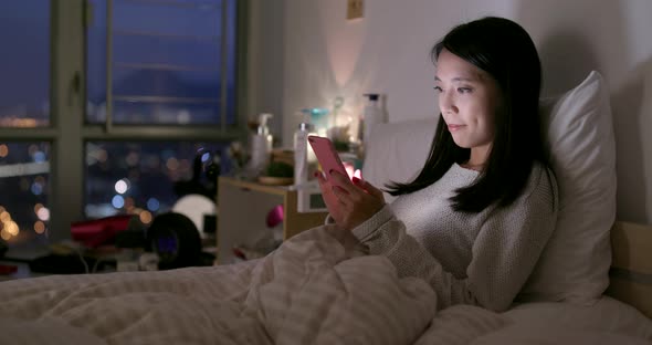 Woman look at mobile phone on bed at night