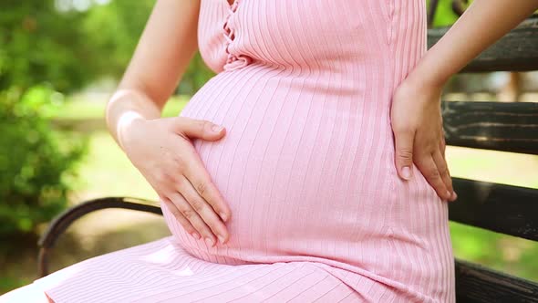 Pregnant Woman Stroking Belly and Holding on to His Back in a Green Park