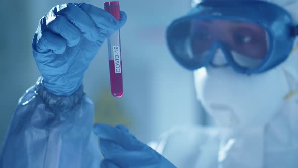 Scientist Examining Blood in Test Tube with Covid-19 Inscription