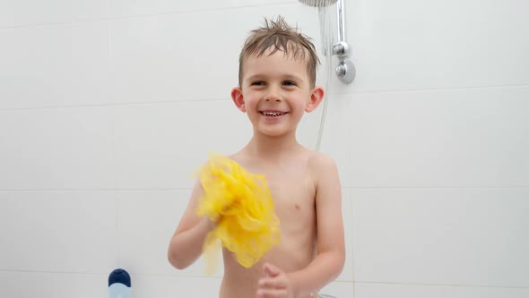 Happy Laughing Boy Playing with Yellow Sponge While Washing Under Shower in Bath