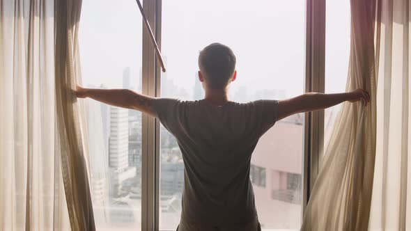 Handsome Man Opening in Slow Motion the Window Curtain on a Sunny Morning in a Hotel Room a Man