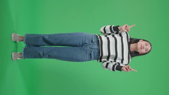 Full Body Of An Asian Woman Pointing Up While Standing In Front Of Green Screen Background