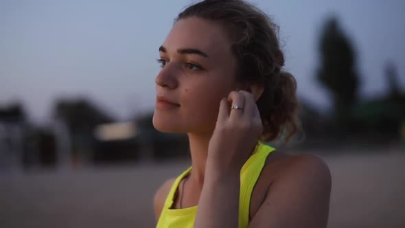 Young Woman Puts on Headphones By the Sea