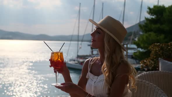 Woman in Straw Hat Drinking Aperol Spritz Cocktail Sitting at Summer Cafe Terrace at Ermioni Greece