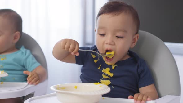 Messy Asian Twins Eating Baby Puree with Spoons