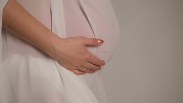 A Naked Pregnant Girl in a White Fabric Holding Her Tummy with Her Hands