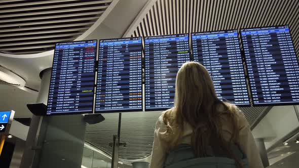 Woman in International Airport Looking at the Flight Information Board.