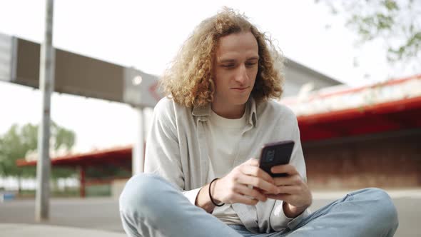 Confident curly-haired man typing by phone