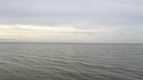 AERIAL: Flying Over Water to Horizon on a Cloudy Dull Day