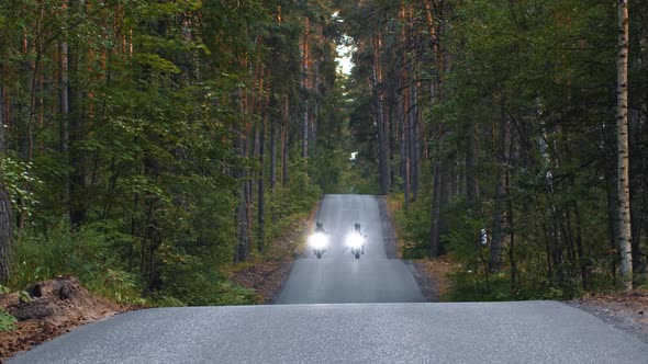 Motor Riding  Two Women in Helmets Riding on Empty Road in the Woods with Turned on Headlights