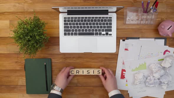 Term crisis is made up of wooden cubes with letters on an office table next to a laptop and work