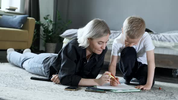 Medium shot mother and child on the floor drawing with magic markers together