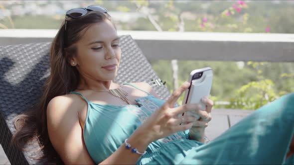 Relaxed Woman Sitting on Lounge Chair and Using Smartphone