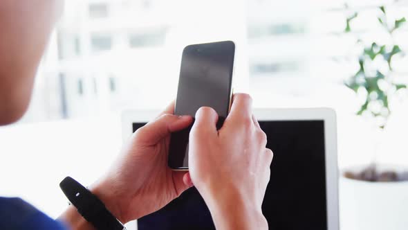 Man in office using phone with laptop and wearing smartwatch