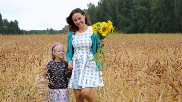 Young Mother with Daughter Walking in Wheat Field
