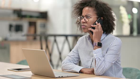 African Businesswoman with Laptop Talking on Smartphone in Office