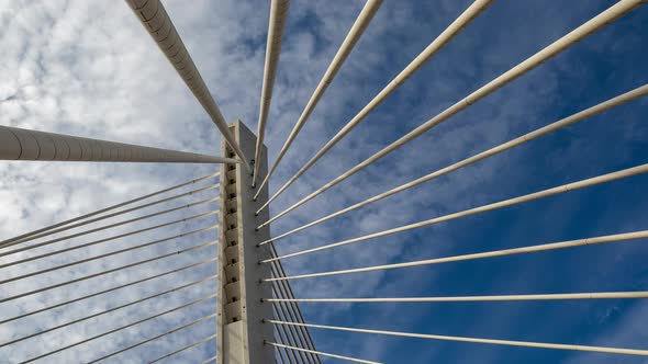 Pylon of a cable stayed bridge under fast moving white clouds in blue sky - lines under tension