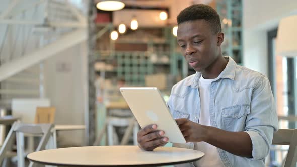 Cheerful Young African Man Working on Tablet in Cafe