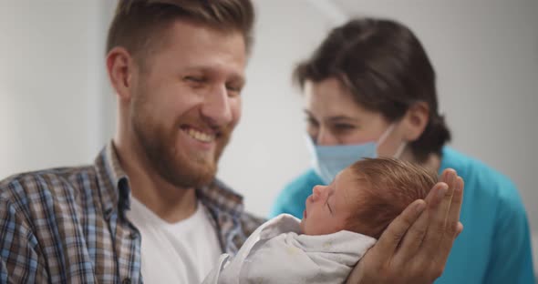 Nurse in Protective Mask Teaching Young Father to Hold Newborn Son