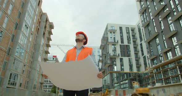 Close-up Portrait of Engineer with Blueprint on Background of Building Under Construction. Young