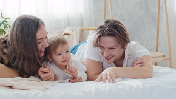 Happy Caucasian Parents with Little Daughter Lie at Home on Bed Laughing Smiling Caring Mother and
