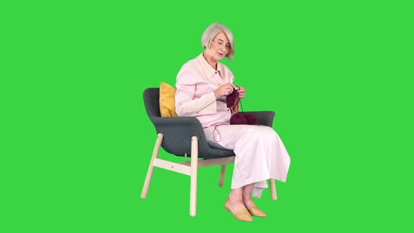 Mature Grandmother Sitting and Knitting and Telling a Story To Camera on a Green Screen Chroma Key