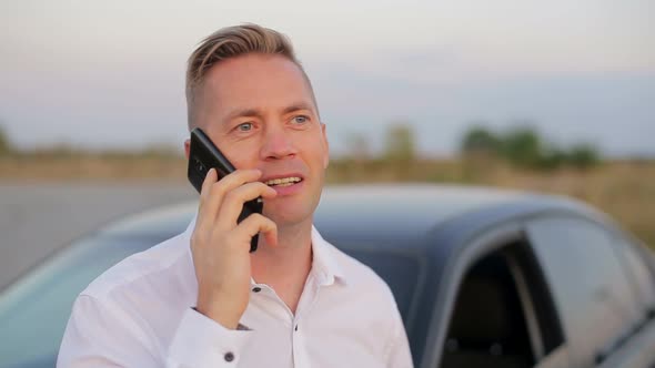 Handsome smiling businessman standing near car and using mobile phone.