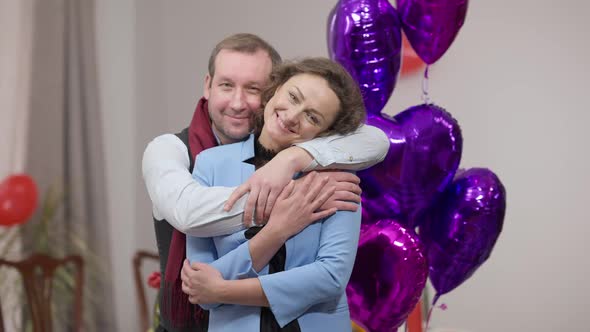 Portrait of Happy Relaxed Beautiful Woman Looking at Camera Smiling As Loving Man Hugging Spouse