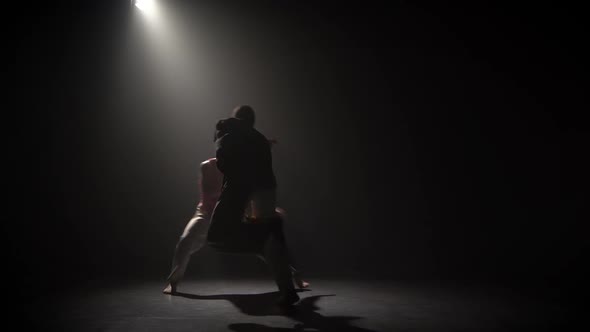 Woman and Man Practicing Capoeira in Darkness Under Spotlight at Studio