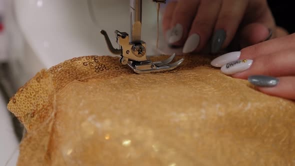 Seamstress Sewing a Dress Made of Gold Openwork Fabric on a Sewing Machine