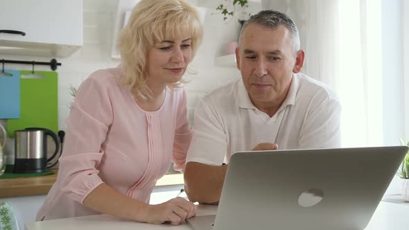 Happy Elderly Family Using Computer in Apartment Kitchen